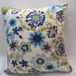 May include: Square decorative pillow with a floral pattern. The pillow features a cream-colored background with a repeating pattern of blue, navy, gray, and green flowers. The pillow's edges are neatly finished, and the overall design is modern and stylish.