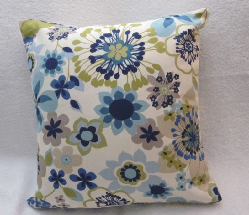 May include: Square decorative pillow with a floral pattern. The pillow features a cream-colored background with a repeating pattern of blue, navy, gray, and green flowers. The pillow's edges are neatly finished, and the overall design is modern and stylish.