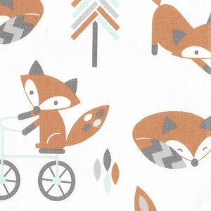 May include: White fabric with a repeating pattern of cartoon foxes in shades of brown, gray, and teal. One fox rides a bicycle. Trees and leaf shapes are also featured in the design.