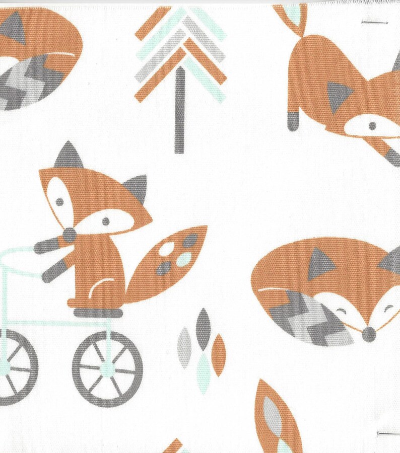 May include: White fabric with a repeating pattern of cartoon foxes in shades of brown, gray, and teal. One fox rides a bicycle. Trees and leaf shapes are also featured in the design.