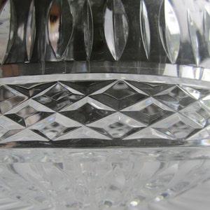 May include: Close-up of a clear crystal bowl with a diamond-cut pattern. The bowl has a rounded shape with a decorative rim and a base with a swirling design. The crystal reflects light, creating a sparkling effect.