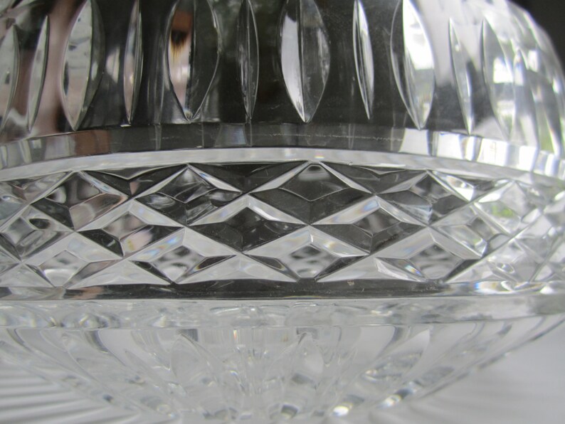 May include: Close-up of a clear crystal bowl with a diamond-cut pattern. The bowl has a rounded shape with a decorative rim and a base with a swirling design. The crystal reflects light, creating a sparkling effect.