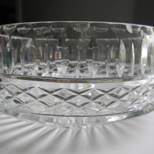 May include: A clear crystal bowl with a diamond-cut pattern on the lower half and vertical cuts on the upper half. The bowl is round and has a scalloped edge. A small gold sticker is visible on the side.