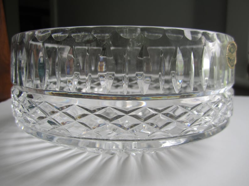 May include: A clear crystal bowl with a diamond-cut pattern on the lower half and vertical cuts on the upper half. The bowl is round and has a scalloped edge. A small gold sticker is visible on the side.