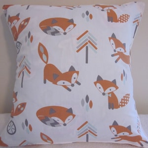 May include: Square white pillow with a repeating pattern of orange foxes, gray trees, and blue-gray leaf shapes. The foxes are in various poses. The pillow is likely for a bed or couch.