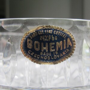 May include: Close-up of a clear crystal bowl with a decorative cut pattern. A blue and gold label reads "HAND CUT LEAD CRYSTAL 24% PbO BOHEMIA MADE IN CZECHOSLOVAKIA". The bowl's surface reflects light, highlighting its intricate design.