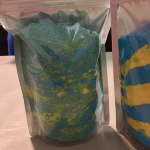 May include: Two clear plastic bags filled with blue and yellow bath salts. The salts are swirled together in a marbled pattern.