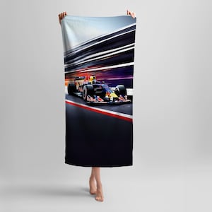 May include: A black and red Formula One racing car speeding down a track with a blurred background. The car has the Red Bull logo on the side. The towel is white with a black and red stripe at the bottom.