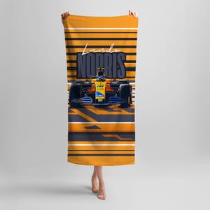 Peut inclure: Serviette de plage orange et noire avec une voiture de course et le texte "Lando Norris" imprimé dessus.
