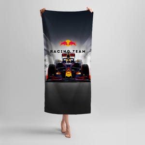 Puede incluir: Una toalla de playa negra con un logotipo del equipo Red Bull Racing y un coche de carreras de Fórmula 1 sobre un fondo blanco y negro.