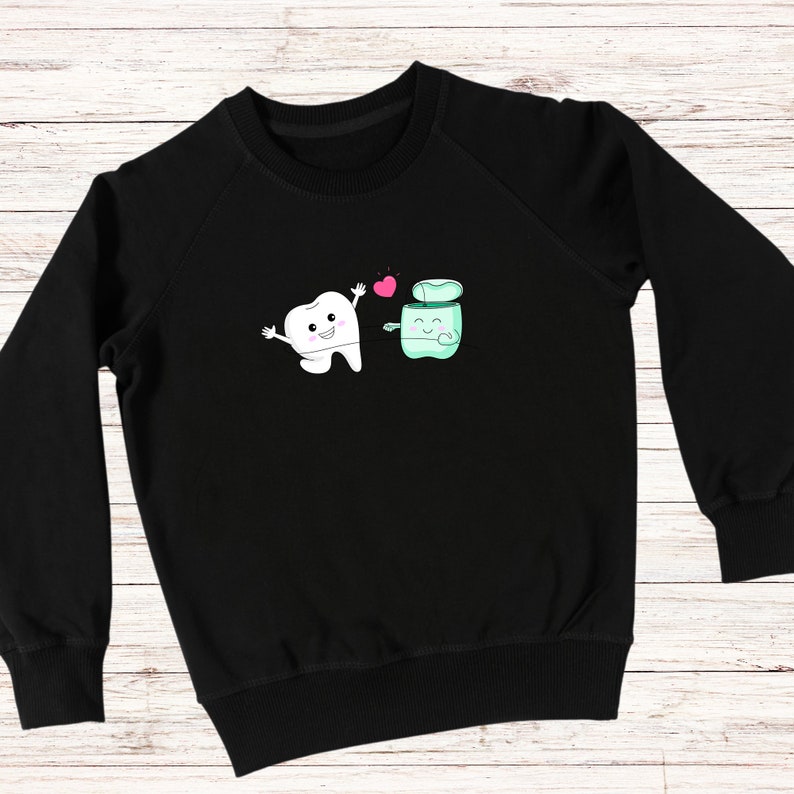 May include: Black sweatshirt with a white tooth and a green floss container graphic. The tooth and floss container are smiling and holding hands. There is a pink heart between them.