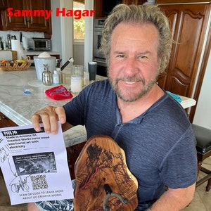 May include: A man holds a wooden guitar stand with a red and brown fractal design. The stand is made by GC Creative Works and features a QR code to learn more about the company. The text "FOX 10" and "Made in Arizona: GC Creative Works turns wood into fractal art with electricity" is visible on the flyer in the man's hand.