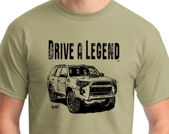 Op de afbeelding: Khaki T-shirt met een zwarte afbeelding van een 4x4 SUV en de tekst "DRIVE A LEGEND". Het ontwerp bevat het "toy rocks" handelsmerk. Het shirt is gemaakt van een zacht, comfortabel materiaal.