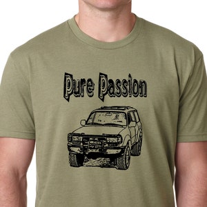 May include: Military green t-shirt with the text "Pure Passion" above a black illustration of a 4x4 vehicle. The shirt is a solid color and has a crew neck.