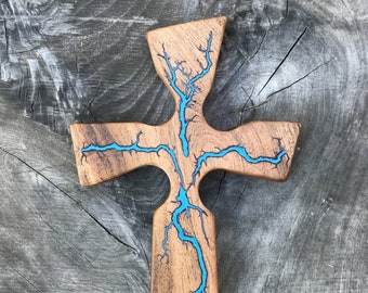 Può includere: Una croce di legno con un'intarsio in resina blu a forma di fulmine. La croce è in legno scuro e ha un aspetto rustico.
