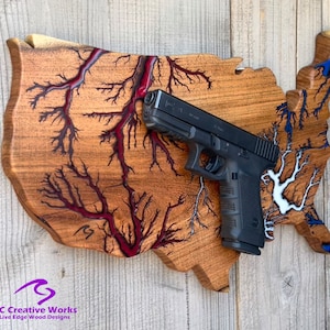 May include: A wooden cutout of the United States of America with red and blue epoxy resin filling the rivers and lakes. A black handgun is mounted on the cutout.