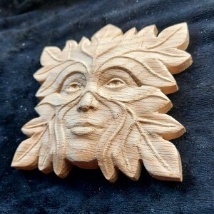 May include: A wooden carving of a Green Man's face, with leaves and branches forming the hair and beard. The carving is detailed and realistic, with a natural wood finish.