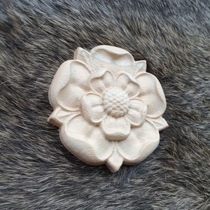 May include: A carved wooden flower with a white finish. The flower has five petals and a center with a raised design.