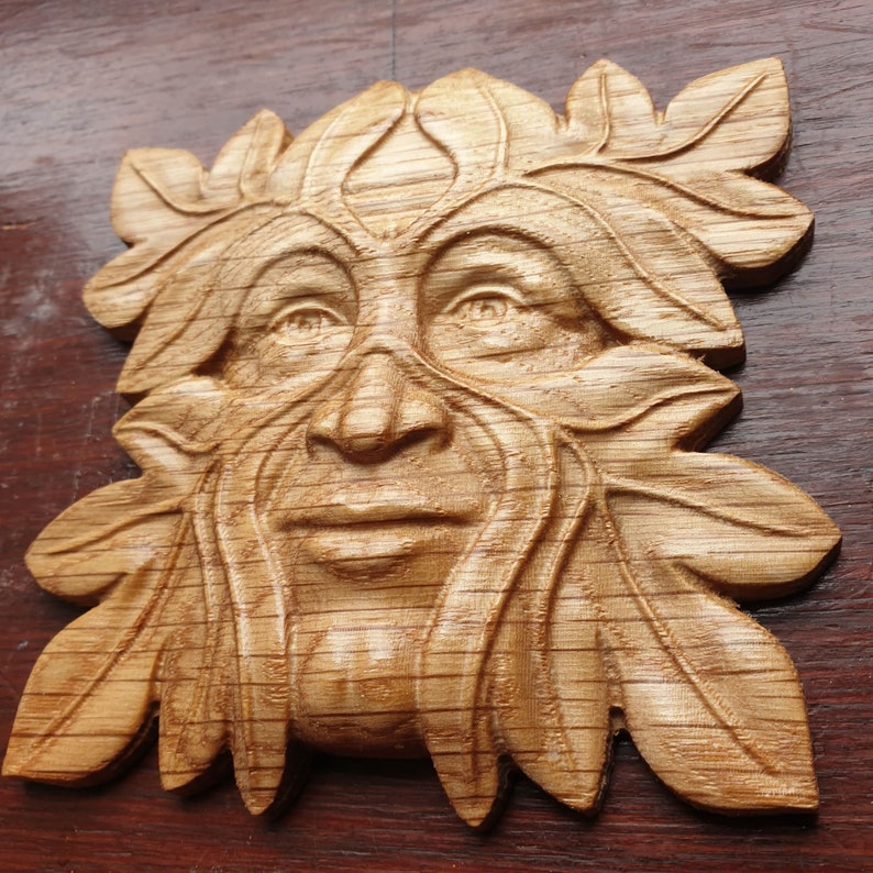 K&ouml;nnte beinhalten: Eine Holzschnitzerei eines Green Man-Gesichts, mit Bl&auml;ttern und &Auml;sten, die Haare und Bart bilden. Die Schnitzerei ist detailliert und realistisch, mit einer warmen braunen Farbe.