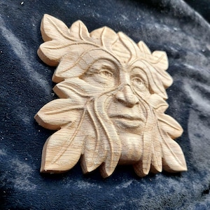 K&ouml;nnte beinhalten: Eine Holzschnitzerei des Green Man, einer mythischen Figur, die oft mit einem menschlichen Gesicht umgeben von Bl&auml;ttern dargestellt wird. Die Schnitzerei ist detailliert und realistisch, mit einer strukturierten Oberfl&auml;che, die den Eindruck von Rinde vermittelt.