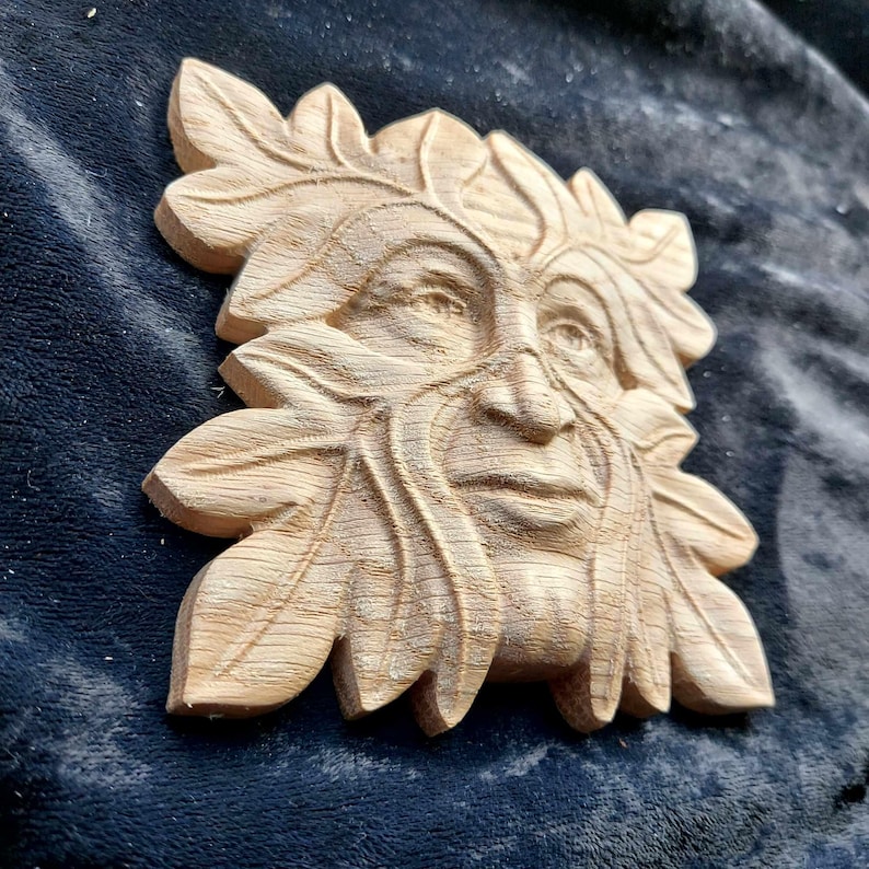 K&ouml;nnte beinhalten: Eine Holzschnitzerei des Green Man, einer mythischen Figur, die oft mit einem menschlichen Gesicht umgeben von Bl&auml;ttern dargestellt wird. Die Schnitzerei ist detailliert und realistisch, mit einer strukturierten Oberfl&auml;che, die den Eindruck von Rinde vermittelt.