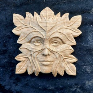 May include: A wooden carving of a Green Man's face, surrounded by leaves. The carving is detailed and realistic, with a serene expression.