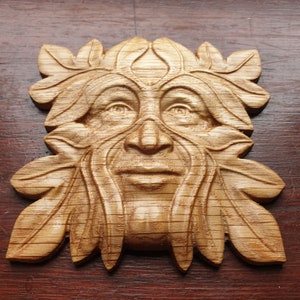 K&ouml;nnte beinhalten: Eine Holzschnitzerei eines Green Man, einer mythischen Figur, die oft mit der Natur und dem Wald in Verbindung gebracht wird. Die Schnitzerei ist detailliert und realistisch, mit einem Gesicht, das von Bl&auml;ttern und &Auml;sten eingerahmt wird.