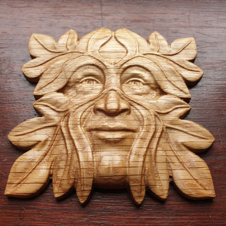 K&ouml;nnte beinhalten: Eine Holzschnitzerei eines Green Man, einer mythischen Figur, die oft mit der Natur und dem Wald in Verbindung gebracht wird. Die Schnitzerei ist detailliert und realistisch, mit einem Gesicht, das von Bl&auml;ttern und &Auml;sten eingerahmt wird.