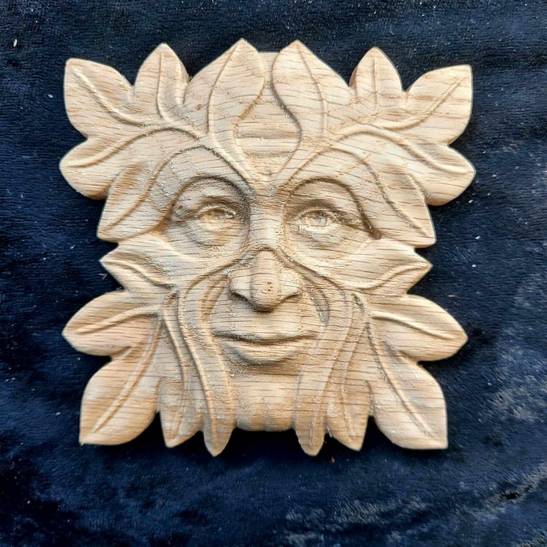 K&ouml;nnte beinhalten: Eine Holzschnitzerei eines Green Man-Gesichts, umgeben von Bl&auml;ttern. Die Schnitzerei ist detailliert und realistisch, mit einem ruhigen Ausdruck.