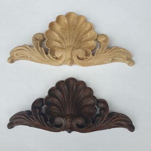 May include: Two ornate wooden decorative pieces with a shell design. The top piece is light wood and the bottom piece is dark wood.