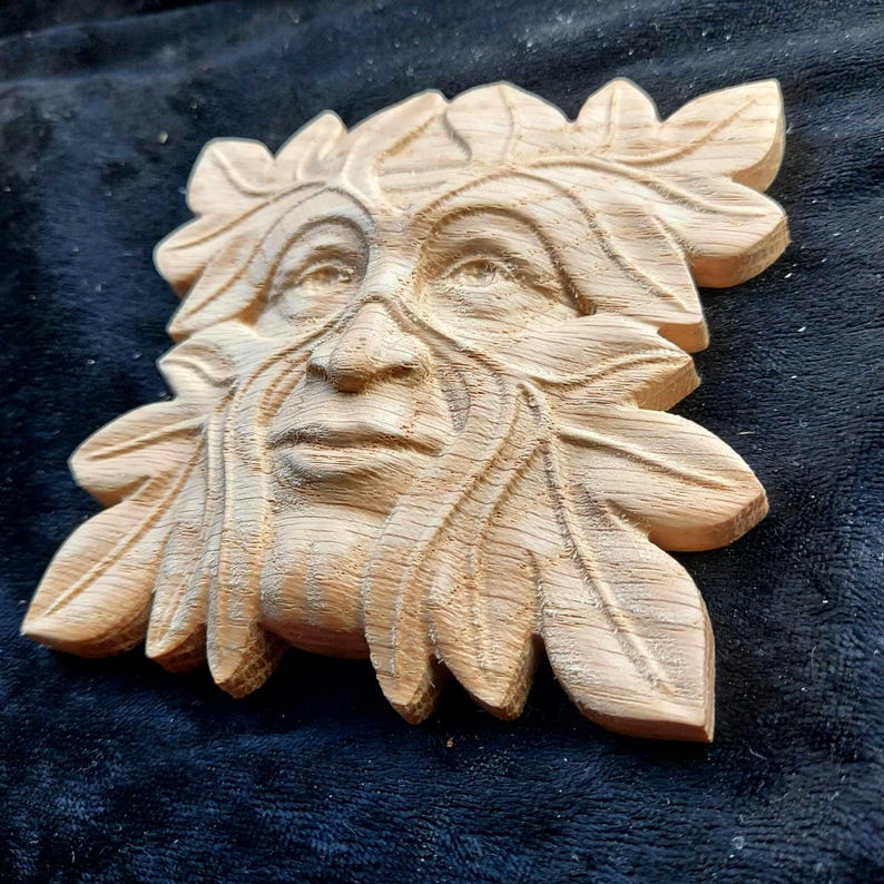 K&ouml;nnte beinhalten: Eine Holzschnitzerei eines Green Man-Gesichts, mit Bl&auml;ttern und &Auml;sten, die Bart und Haare bilden. Die Schnitzerei ist detailliert und realistisch, mit einem ruhigen Ausdruck.