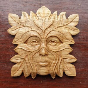 May include: A wooden carving of a Green Man's face, surrounded by leaves. The carving is detailed and realistic, with a warm brown color.
