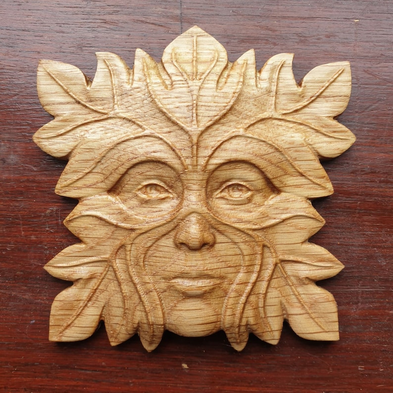 May include: A wooden carving of a Green Man's face, surrounded by leaves. The carving is detailed and realistic, with a warm brown color.