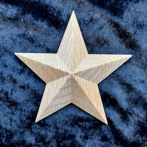 May include: A five-pointed wooden star, made from light-coloured wood. The star has a textured surface and is set against a dark blue background. The star's design features detailed carved lines, adding depth and dimension to the piece.