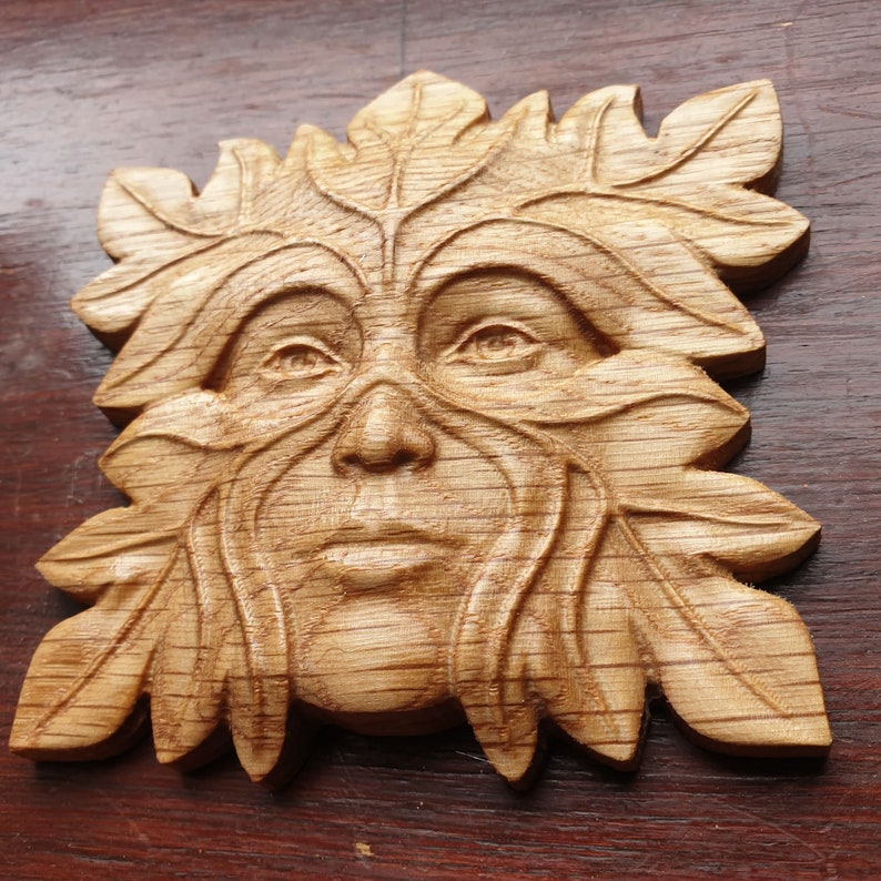 May include: A wooden carving of a Green Man's face, surrounded by leaves. The carving is detailed and realistic, with a natural wood finish.
