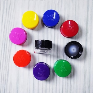 May include: Assortment of colorful bottle caps with a butterfly design. The caps are red, blue, yellow, green, purple, and pink. There is also a clear glass bottle with a black lid.