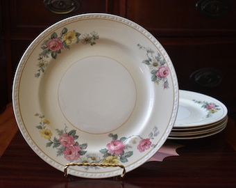 May include: Set of six white dinner plates with a gold rim and floral pattern featuring pink, yellow, and green roses.