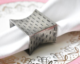 May include: Silver napkin ring with a textured, hammered finish. The ring is curved and has a modern design.