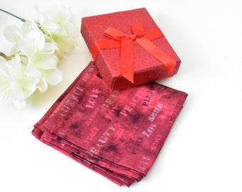 Puede incluir: Una caja de regalo roja con una cinta y un lazo rojos, junto a un cuadrado de tela roja con las palabras "Peace, Love, Smile" impresas.