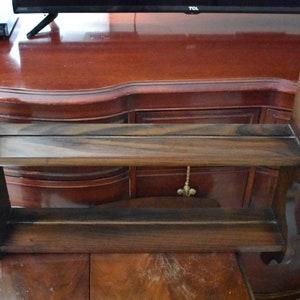 May include: A dark brown wooden shelf with two shelves. The shelf is mounted on a wall and has a decorative design on the front.