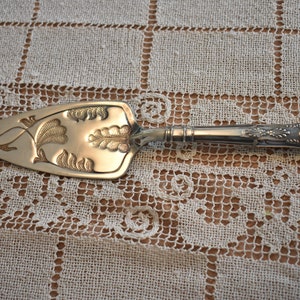May include: Silver cake server with an ornate floral design. The handle is decorated with a scroll design.