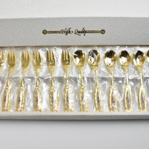 Könnte beinhalten: Ein Set mit 12 goldfarbenen Teelöffeln und Gabeln in einer weißen Box mit dem Aufdruck "High Quality" auf dem Deckel. Die Löffel und Gabeln haben ein florales Design.