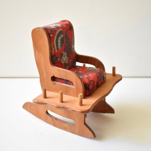 May include: A wooden rocking chair with a red floral patterned cushion. The chair is made of light brown wood and has a simple design.