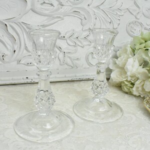 Könnte beinhalten: Zwei klare Glaskerzenhalter mit Diamantenmuster. Die Kerzenhalter stehen auf einer weißen Oberfläche.