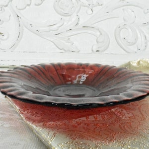 Puede incluir: Un cuenco de cristal rojo rub&iacute; con borde ondulado. El cuenco tiene un borde oscuro y un interior texturizado. El cuenco est&aacute; sobre una superficie estampada, con un fondo de madera blanca tallada.
