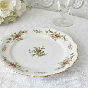 May include: A white porcelain plate with a gold rim and a floral design featuring pink roses and green leaves.