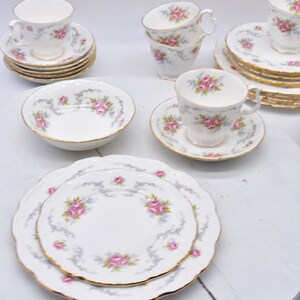 Puede incluir: Un juego de tazas de té y platillos blancos con un patrón floral. Las tazas y los platillos tienen un borde dorado. También hay un tazón blanco con un patrón floral y un borde dorado.