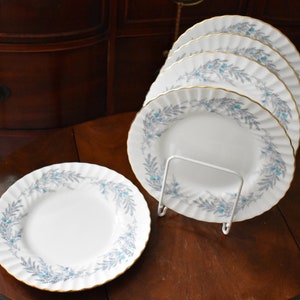 May include: Set of four white ceramic dinner plates with a blue and grey floral pattern and gold trim.