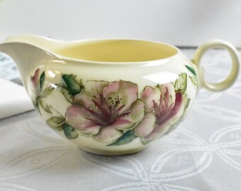 Könnte beinhalten: Cremefarbener Keramik-Sahnegießer mit floralem Design. Der Sahnegießer hat einen Ausguss, einen Henkel und ist mit rosa und grünen Blumen verziert. Der Innenraum ist hellgelb.