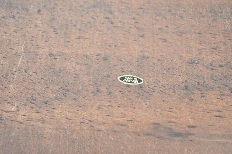 Pode incluir: Close-up de uma superf&iacute;cie de madeira marrom com um adesivo oval preto que diz "Made in Japan".